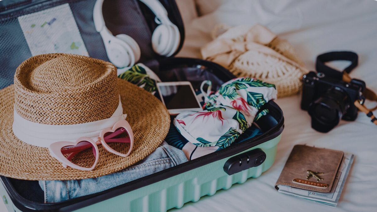 Flat lay of a minimalist travel scene: open suitcase on a bed, neatly packed clothes, reusable water bottle, slim wallet with a few cards, and a small notepad titled “Smart Travel Spending,” in soft natural light with warm neutral tones.