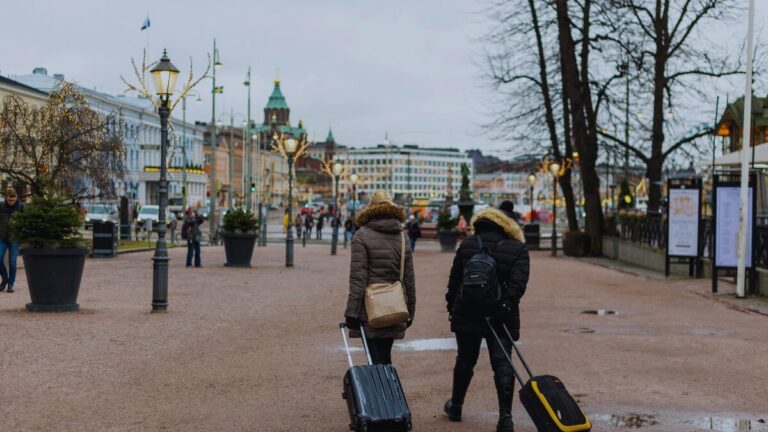 Travelers walking through crowded city street with luggage while watching belongings and surroundings carefully