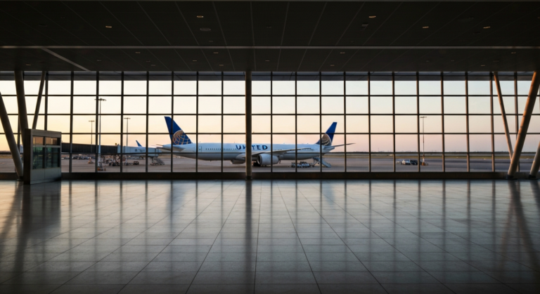Modern airport terminal interior with a United Airlines plane on the tarmac at sunrise