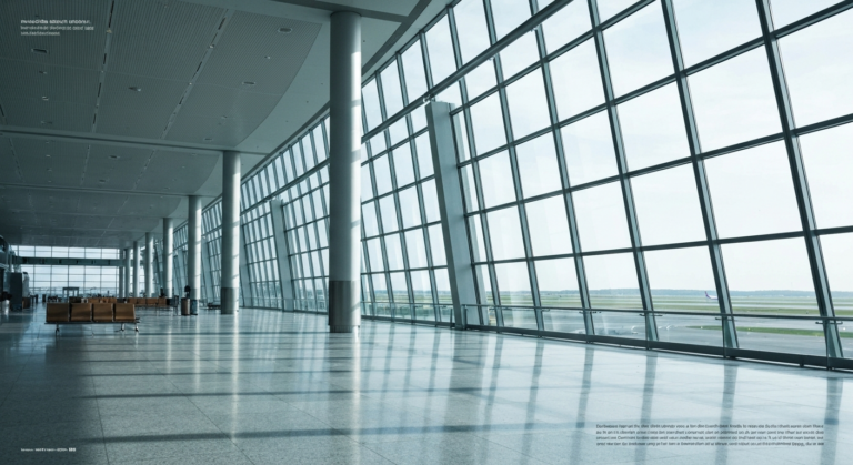 Sleek, modern airport terminal architecture with bright natural light and runway view, no passengers present.