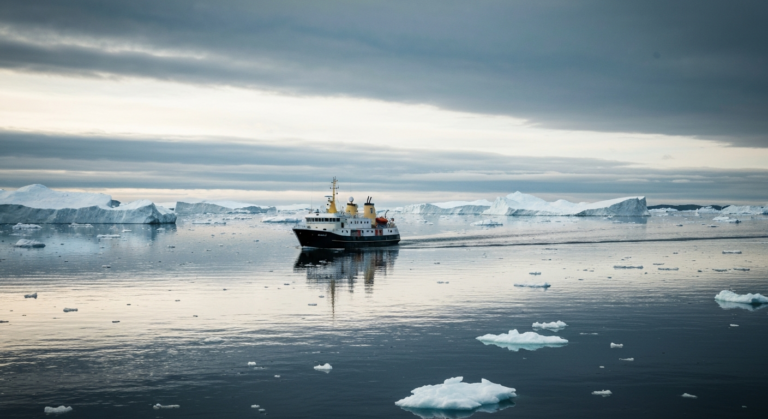 Expedition cruise ship navigating pristine Arctic waters surrounded by icebergs at sunset