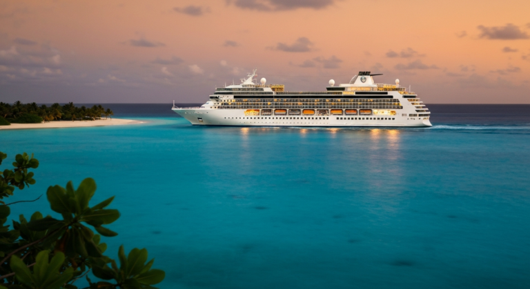 Luxury P&O cruise ship sailing through calm Caribbean waters near a tropical beach at sunset